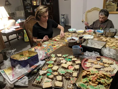 Two women decorate a large array of cookies laid out on a table.