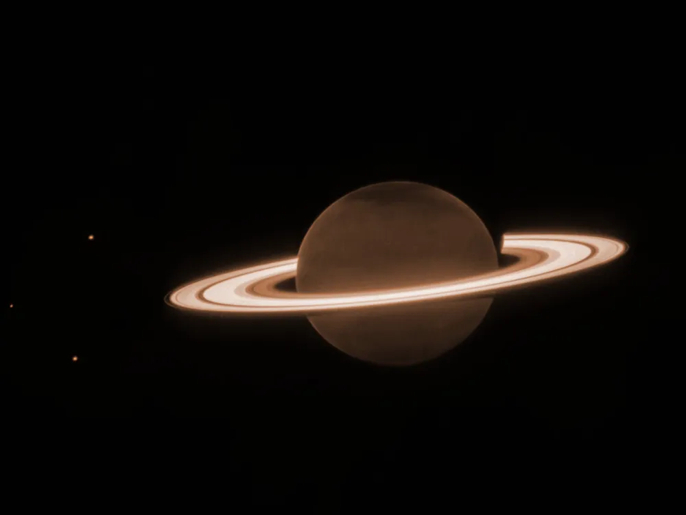 Saturn, with its rings appearing brighter than the planet and three moons to the left of the planet.