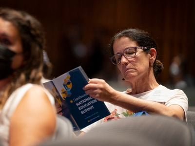 Woman with brown hair and glasses reads through a print program with the words "Smithsonian National Education Summit"